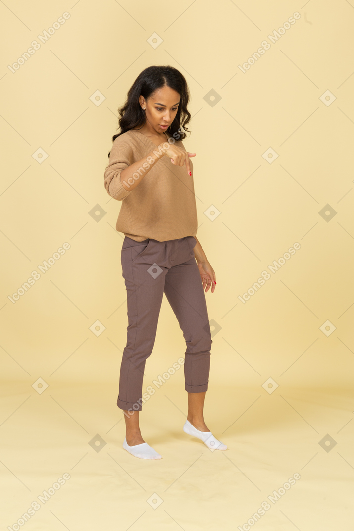 Three-quarter view of a dark-skinned young female pointing finger down