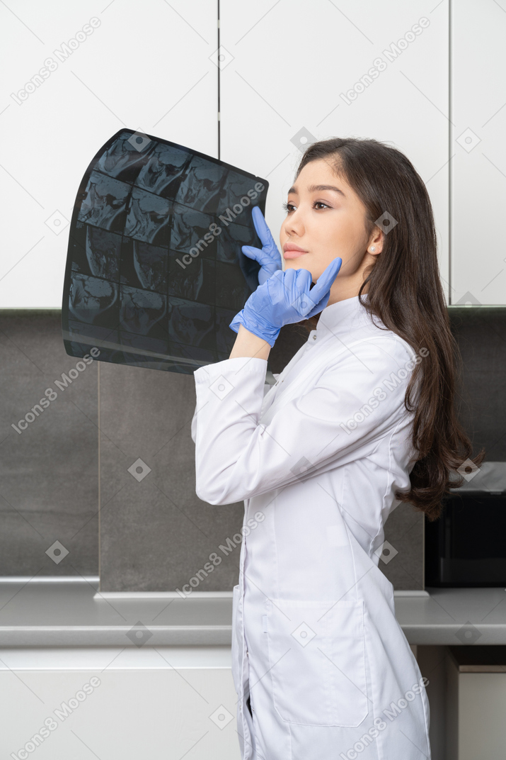 Vista lateral de uma médica segurando uma imagem de raio-x e olhando esperançosamente para o lado