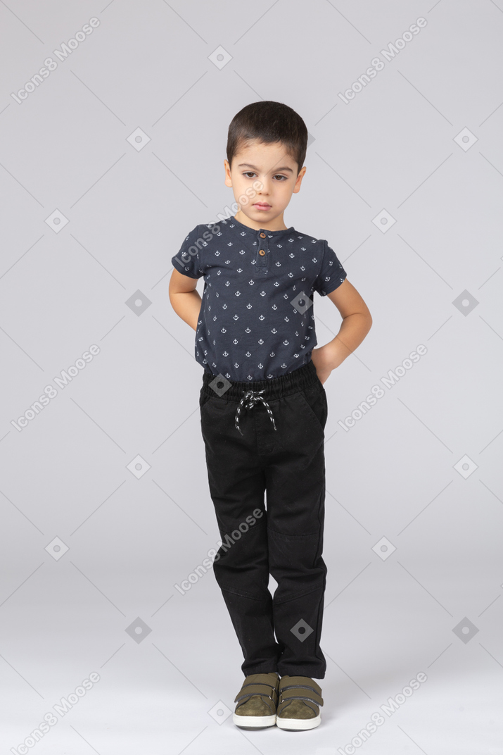 Front view of a cute boy in casual clothes posing with hands behind back