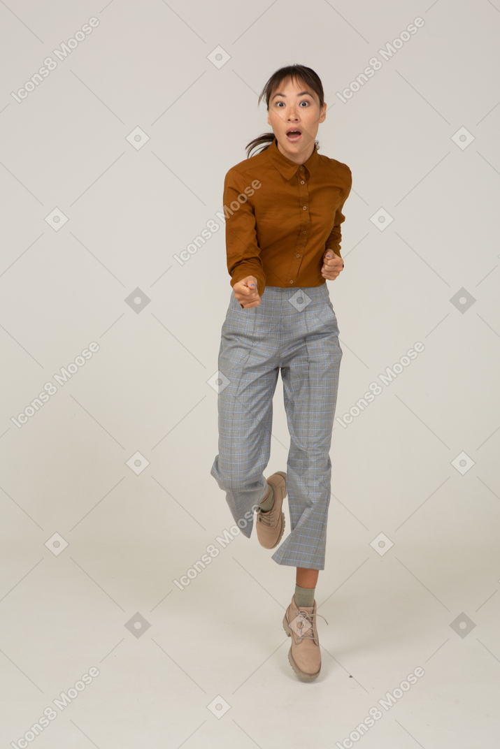 Vista frontal de uma jovem fêmea asiática pulando de calça e blusa estendendo as mãos