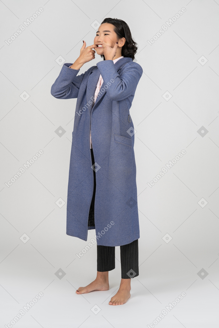 Frau im blauen mantel, die ihren mund streckt und zähne zeigt