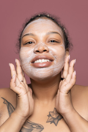 Delighted woman applying creamy face mask