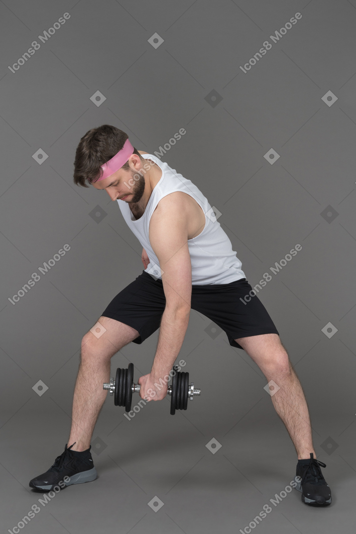 Sporty young man lifting weights in gym