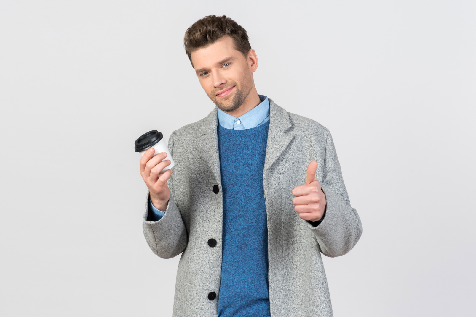 Handsome young man holding coffee and showing thumb up