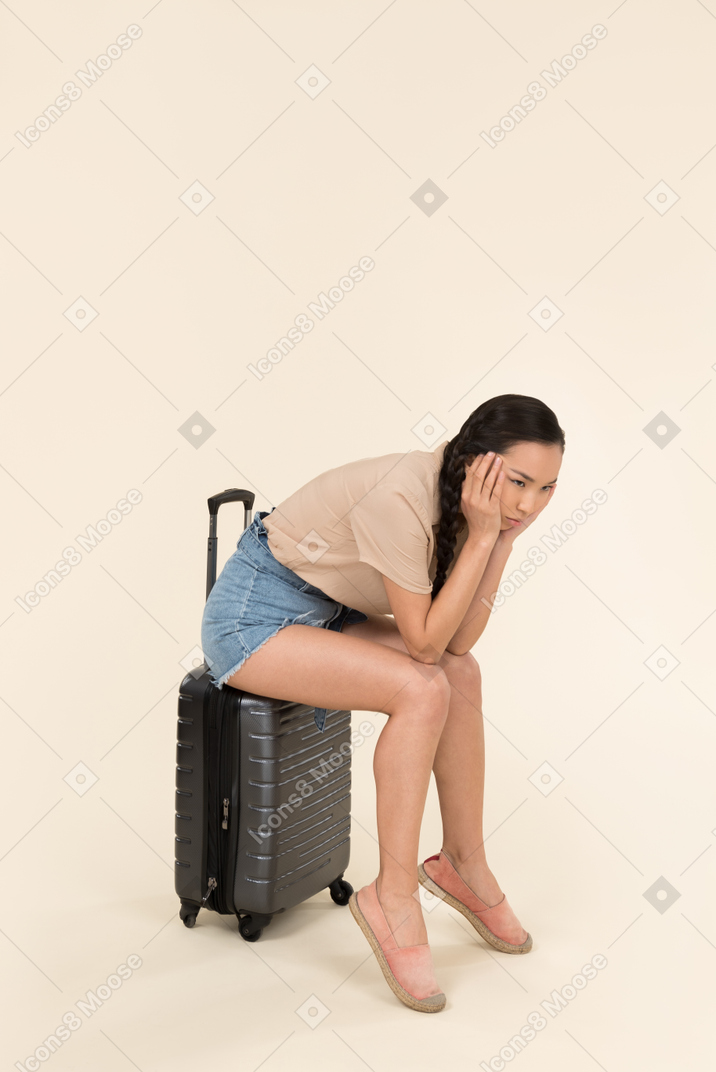 Tired looking young female sitting on suitcase