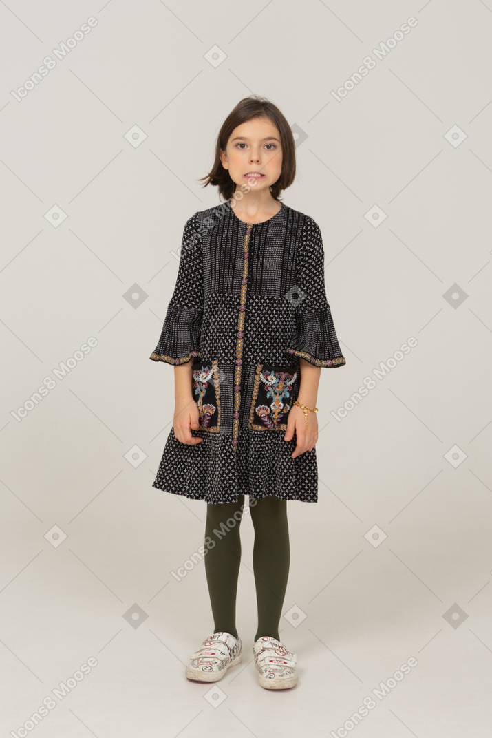 Вид спереди раздраженной маленькой девочки в платье, смотрящей в камеру