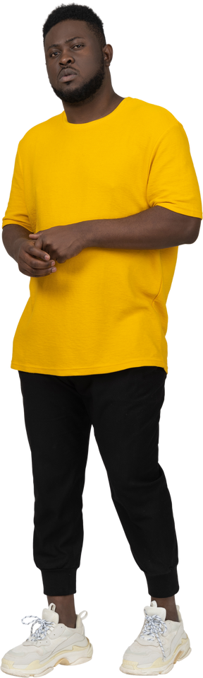 Front view of a young dark-skinned man in yellow t-shirt holding hands together