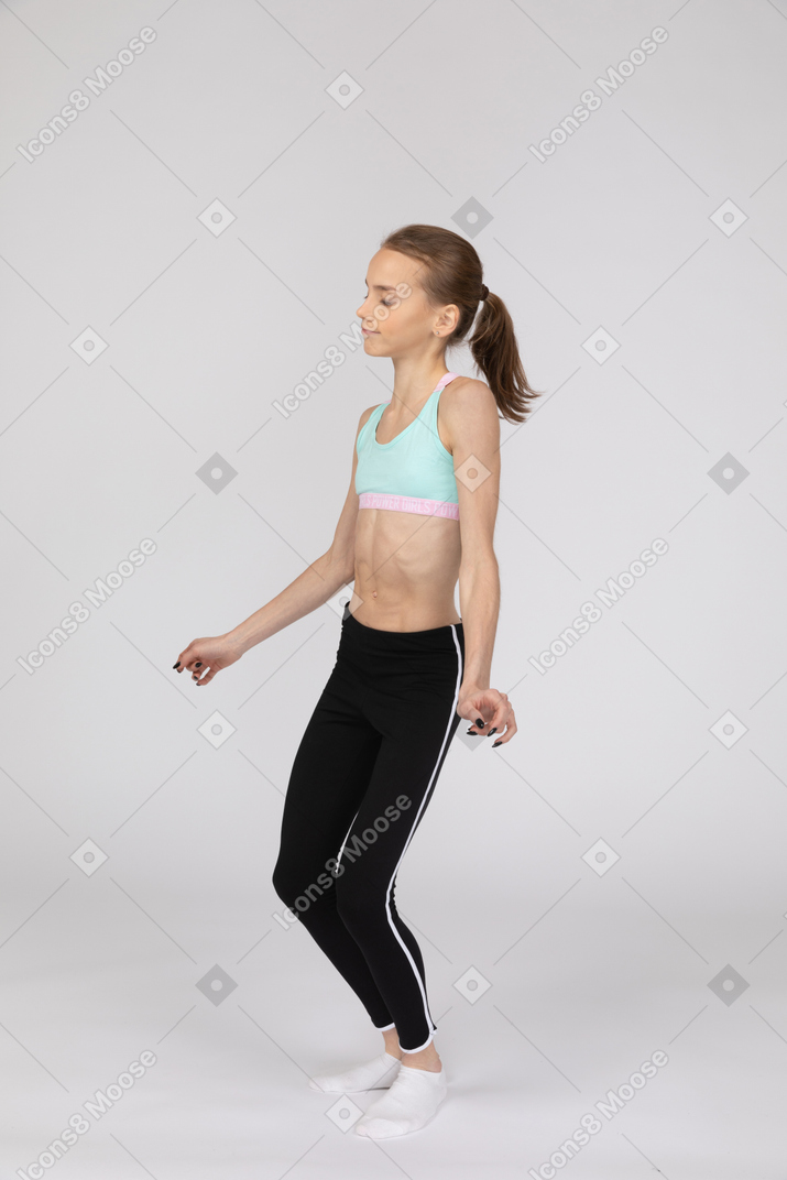 Three-quarter view of a teen girl in sportswear outspreading hands and bending knees
