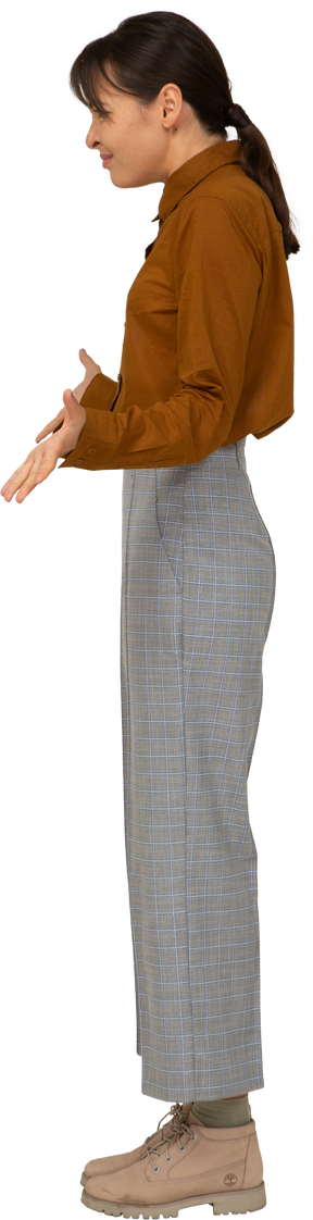 Vista laterale di una giovane donna asiatica in calzoni e camicetta che allarga le braccia