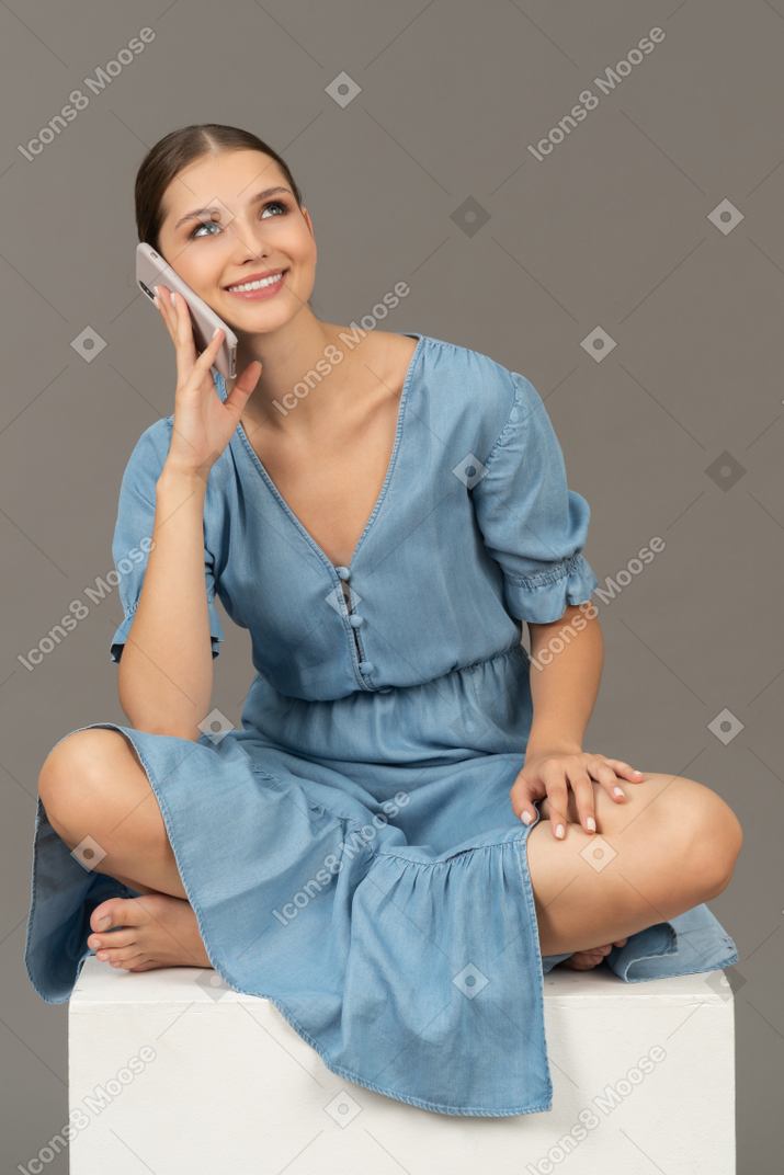 年轻女子坐在立方体上，用智能手机说话的正面图