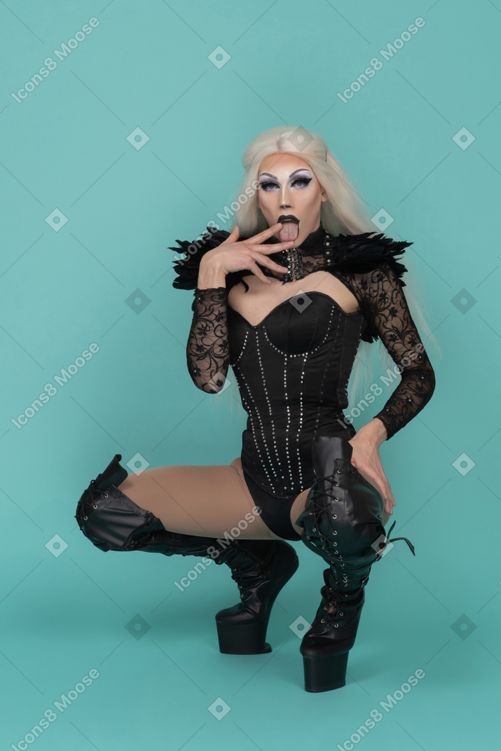 Drag queen agachada mostrando a língua entre os dedos