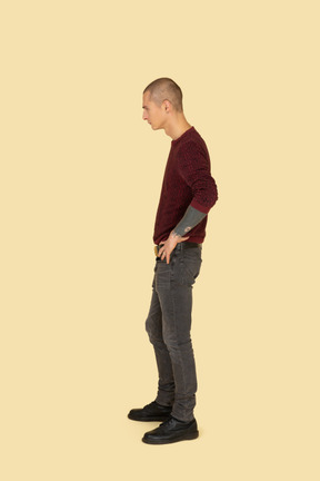 Side view of a young man in pullover putting hands on hips