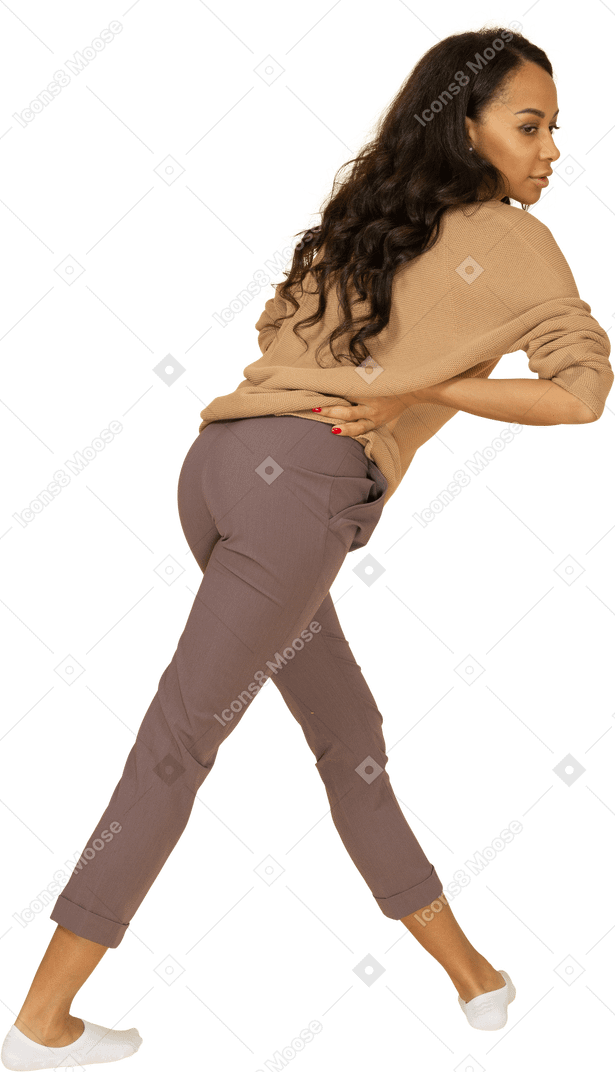 深色皮肤的年轻女性，将手放在臀部上同时向前倾斜的四分之三后视图