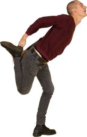 Вид сбоку на молодого человека в красном пуловере, растягивающего ногу