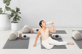 A woman sitting on a mat drinking from a bottle