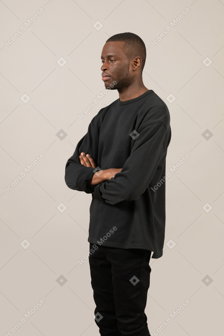 Side view of a calm young guy standing with arms crossed