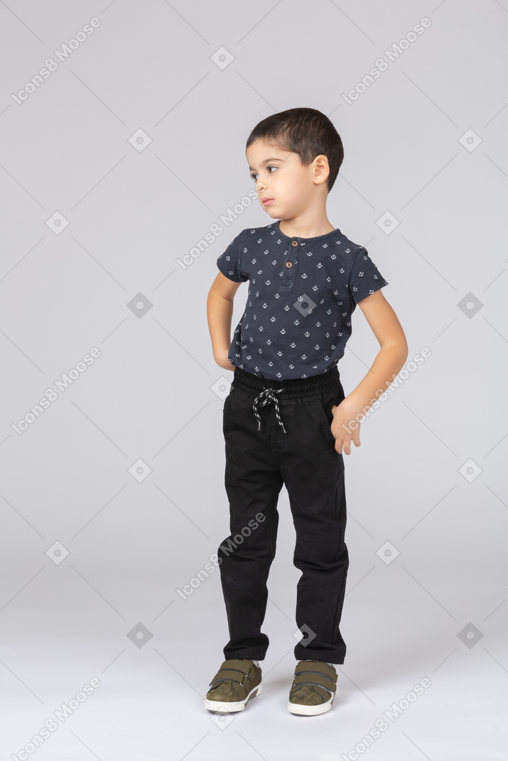一个穿着休闲服的可爱男孩的前视图，双手叉腰，望向一边