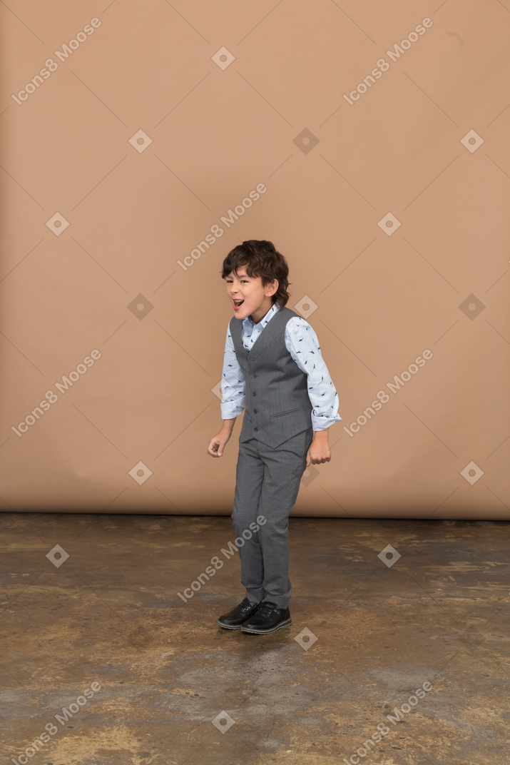 Сердитый мальчик в костюме, стоящий со сжатыми кулаками