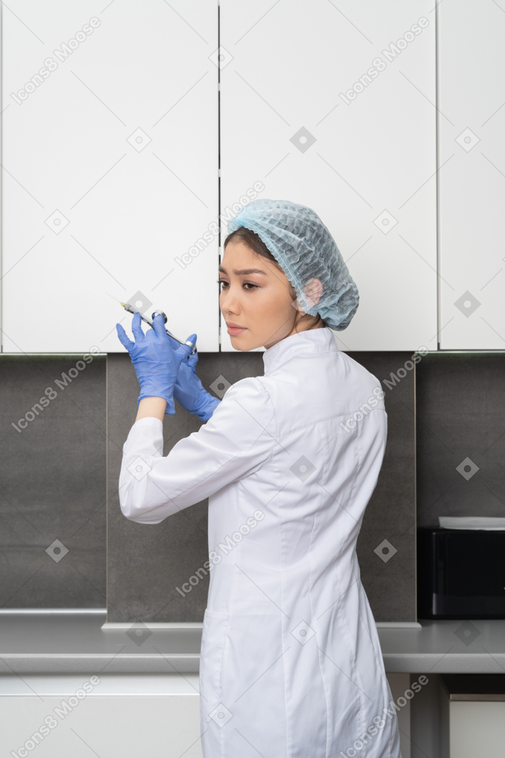 Back view of a nurse in a medical hat holding a syringe and looking aside