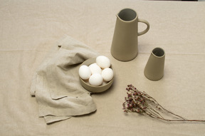 A bowl of chicken eggs and some jars on a grey tablecloth