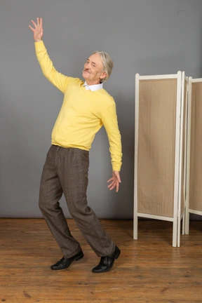Three-quarter view of a smiling old man raising hand while leaning back