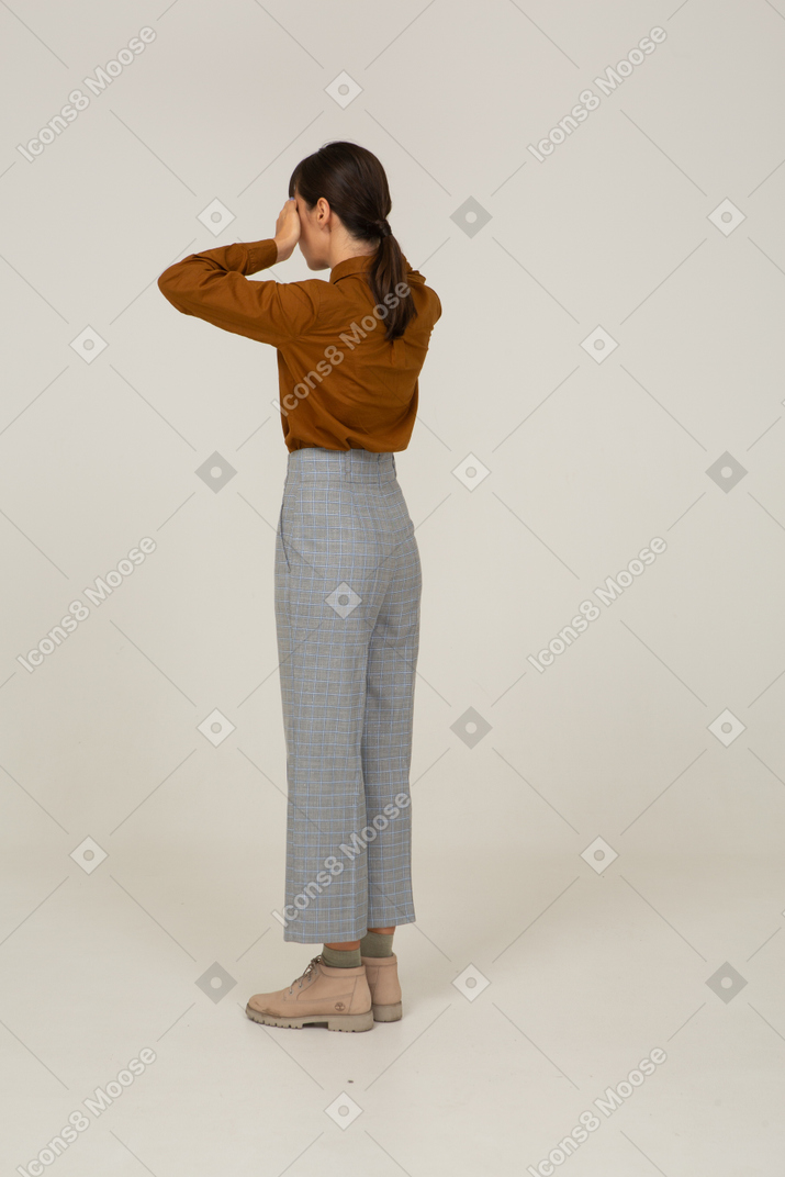 Vista posteriore di tre quarti di una giovane donna asiatica in calzoni e camicetta che nasconde gli occhi