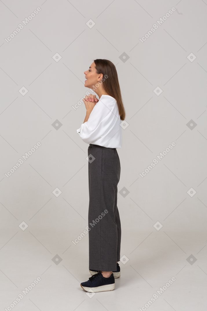 Vista lateral de uma jovem animada com roupa de escritório, de mãos dadas