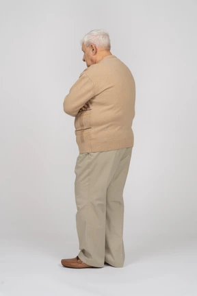 Side view of an old man in casual clothes standing with crossed arms