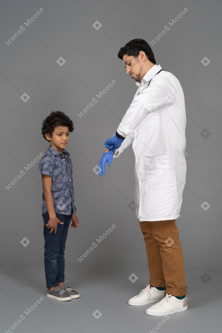 Doctor putting on surgical gloves while boy looking