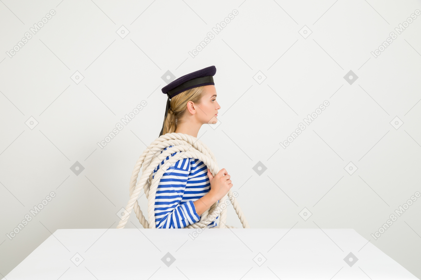 Mujer marinera sentada de perfil con una cuerda por encima del hombro.