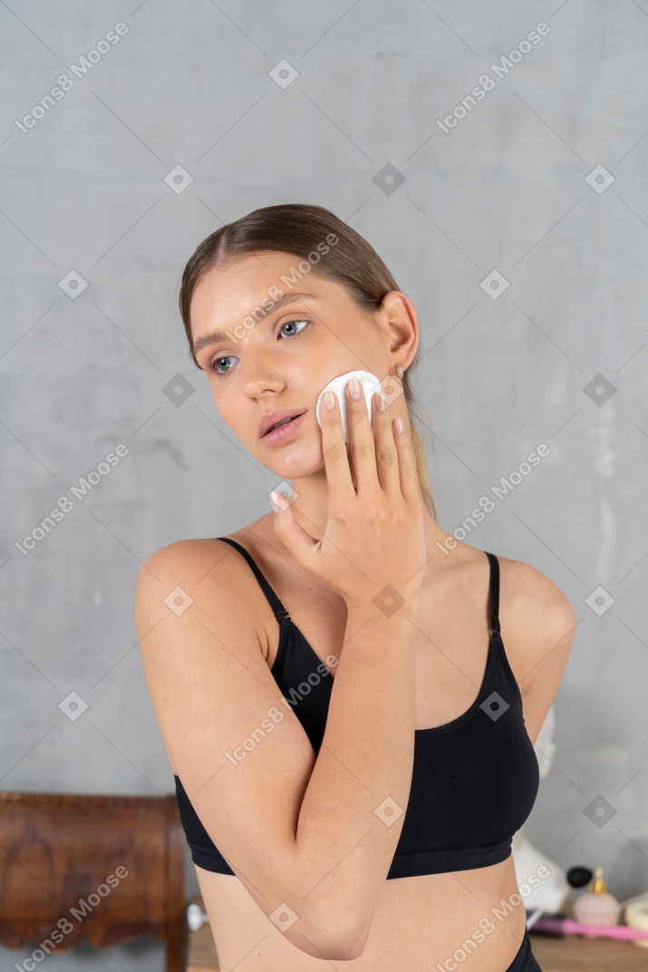 Mujer joven limpiando la cara con una almohadilla de algodón