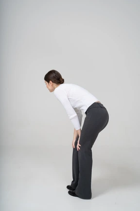 Side view of a woman in black pants and white blouse bending down