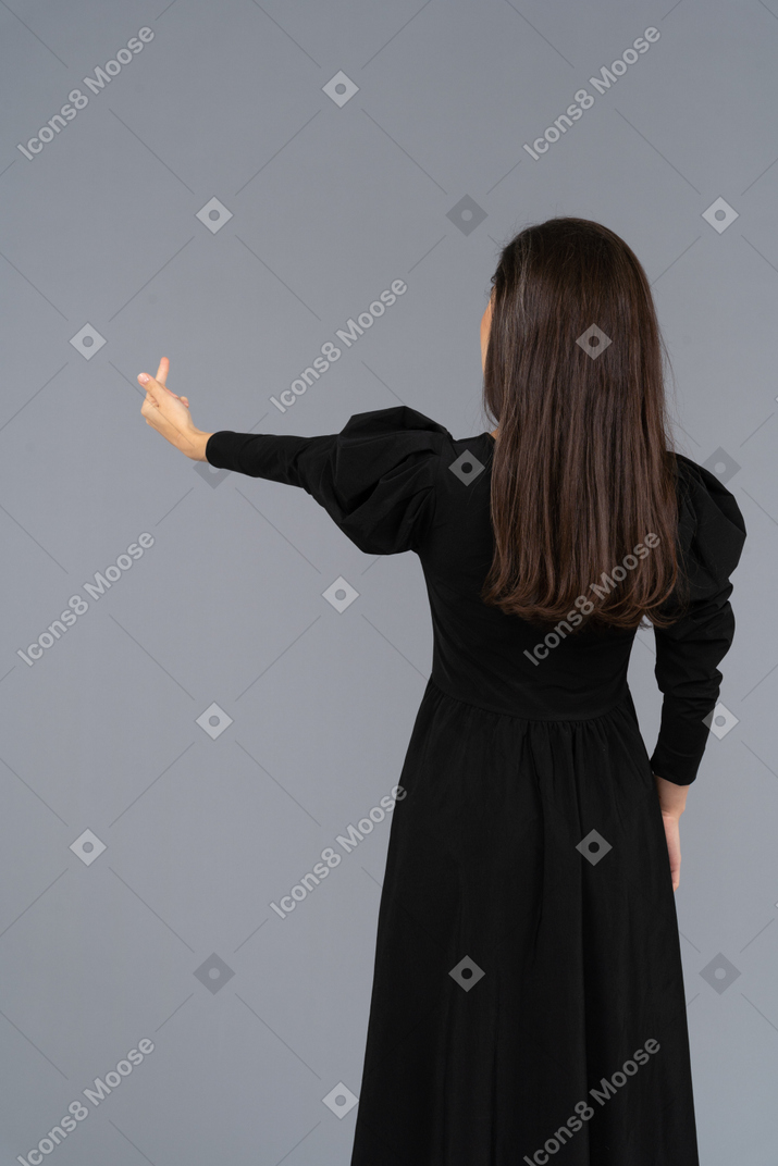 Vista traseira de uma jovem em um vestido preto levantando a mão