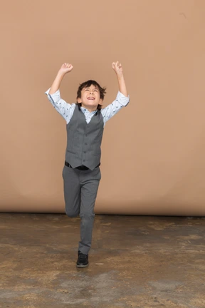 Front view of a cute boy in suit jumping with outstretched arms