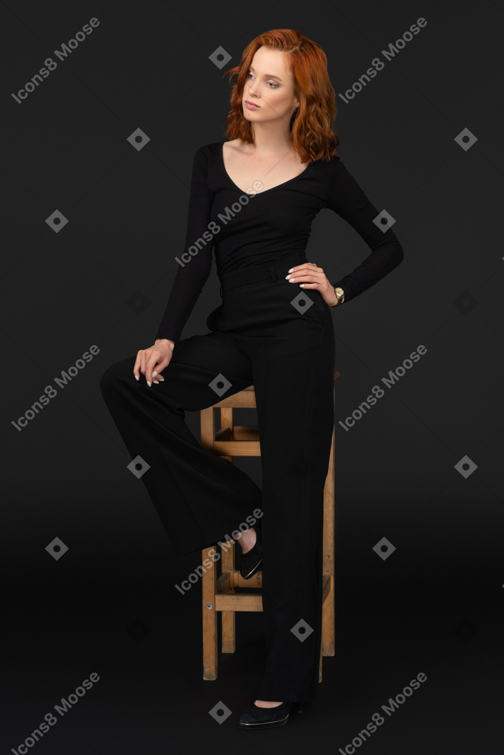 A three-quarter side view of the beautiful woman sitting on the wooden chair and holding her hand on the knee
