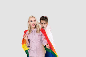 Man standing behind a blond person with rainbow flag
