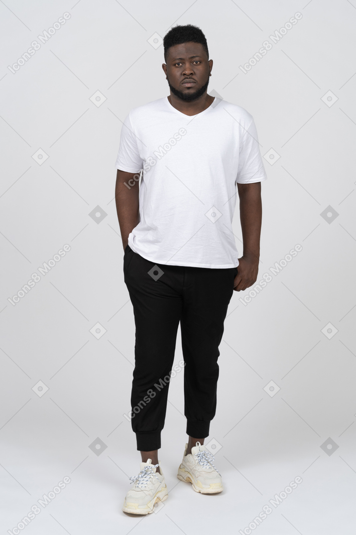 Vista frontale di un giovane uomo dalla pelle scura con una maglietta bianca in piedi immobile
