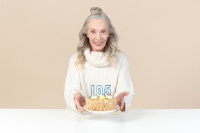 Пожилая женщина держит торт на сто пятый день рождения