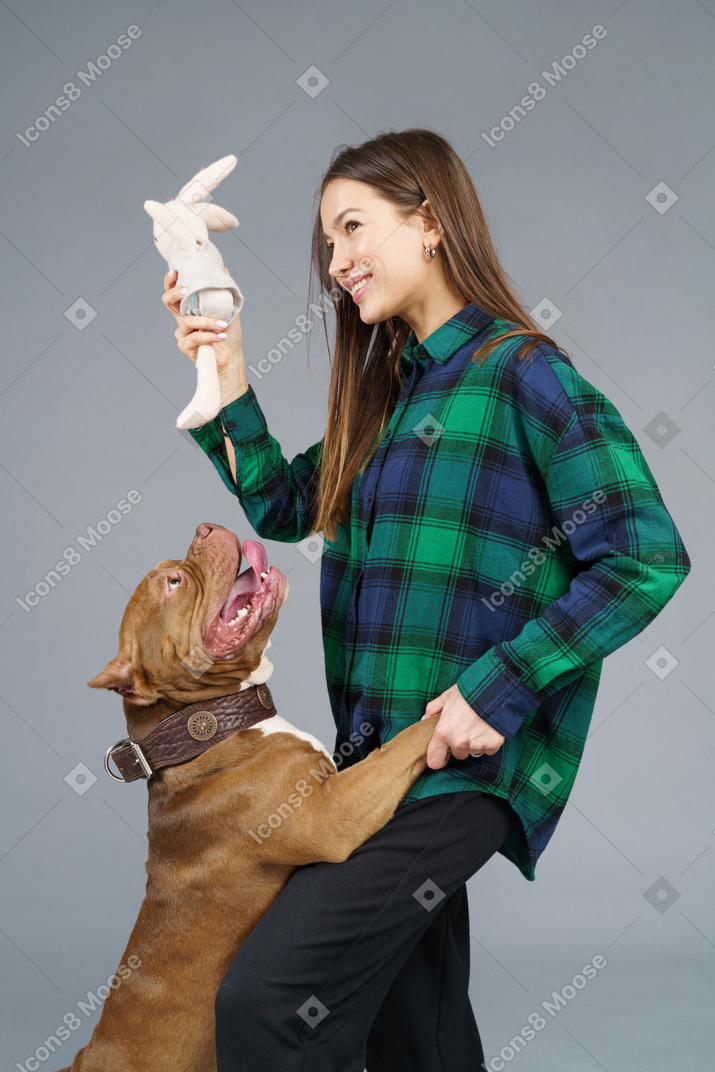 Close-up de um bulldog marrom brincando com uma dona sorridente, olhando para o lado e sorrindo enquanto segura um brinquedo