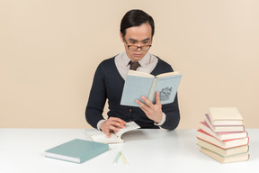 Junger asiatischer student in einer strickjacke ein buch lesend