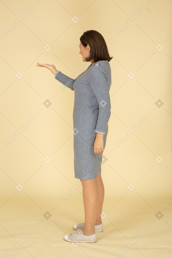 Женщина в сером платье жестикулирует, вид сбоку