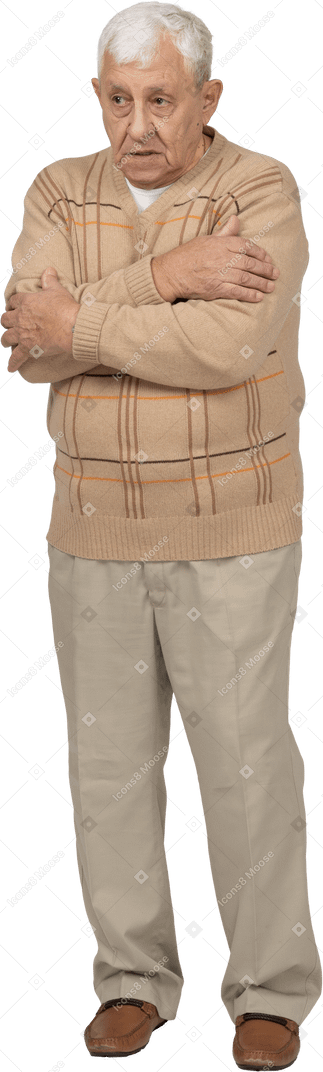 Front view of a scared old man in casual clothes hugging himself