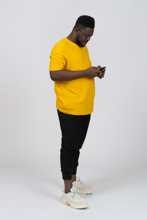 Three-quarter view of a young dark-skinned man in yellow t-shirt chatting via phone