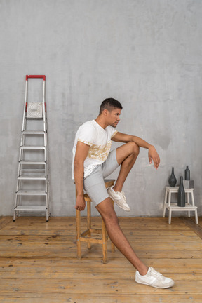 Side view of young man sitting on stool and looking forward