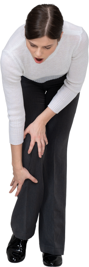 Vista frontal de una mujer joven en ropa de oficina tocando la rodilla