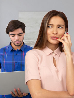 A woman talking on a cell phone next to a man holding a laptop