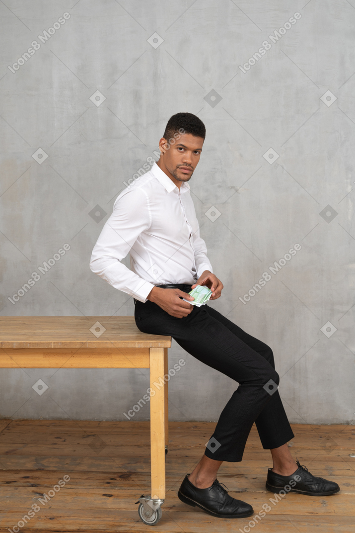 Homem em roupas formais, sentado em uma mesa e segurando dinheiro