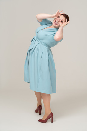 Side view of a woman in blue dress looking through imaginary binoculars