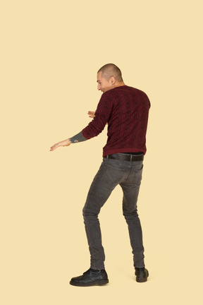 Back view of a scared unwilling young man dressed in red pullover outstretching his hands