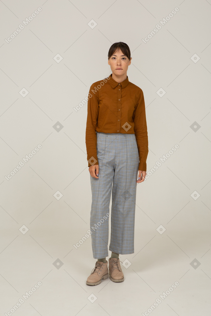 Vista frontal de uma jovem mulher asiática de calça e blusa mordendo o lábio